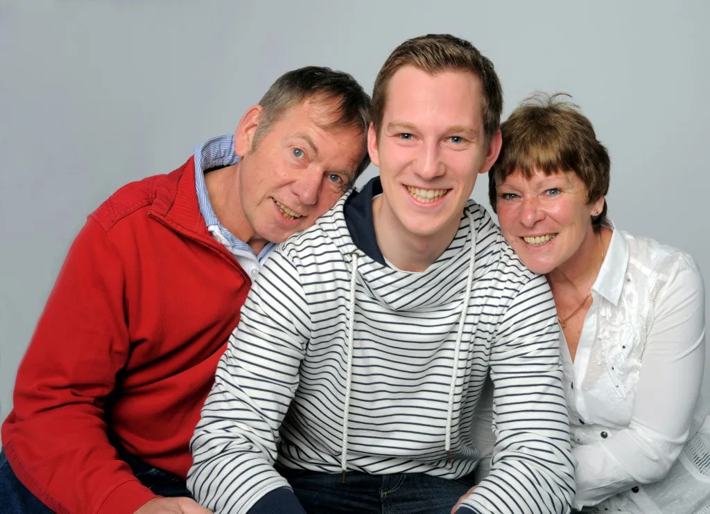 Familienportrait mit Eltern und erwachsenem Sohn vor grauem Studiohintergrund