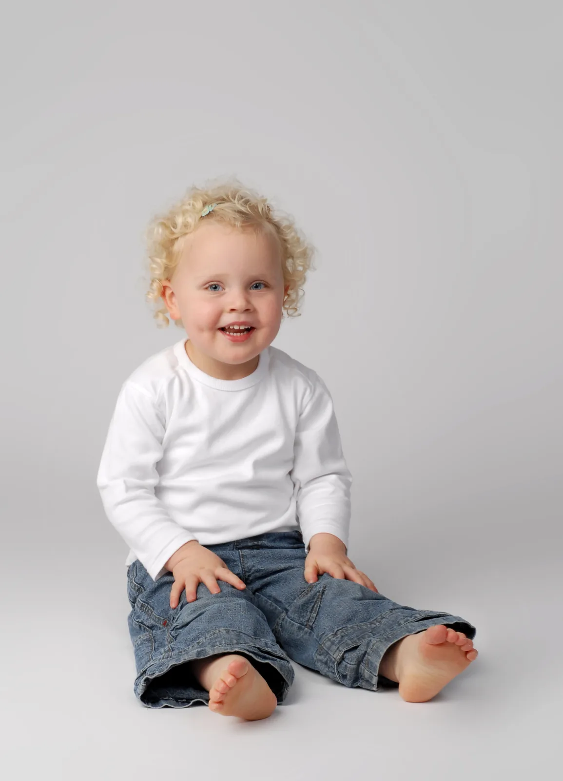Kleinkind mit blonden Locken sitzt lachend im Studio